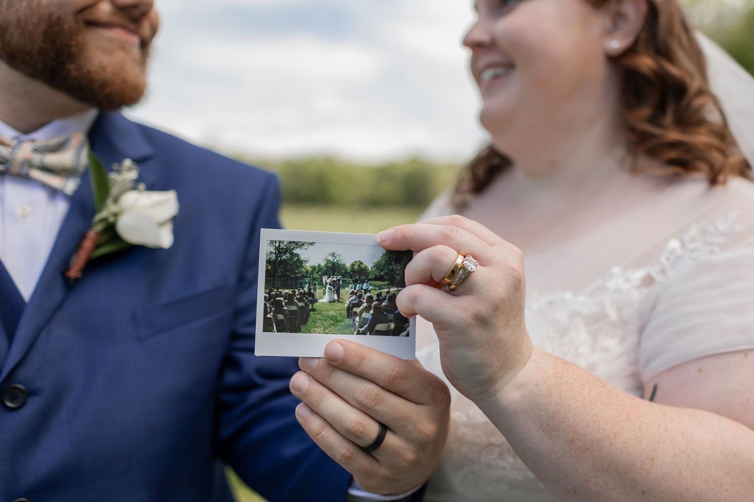 A couple in wedding attire hold a Polaroid photo outdoors during their special day celebration.