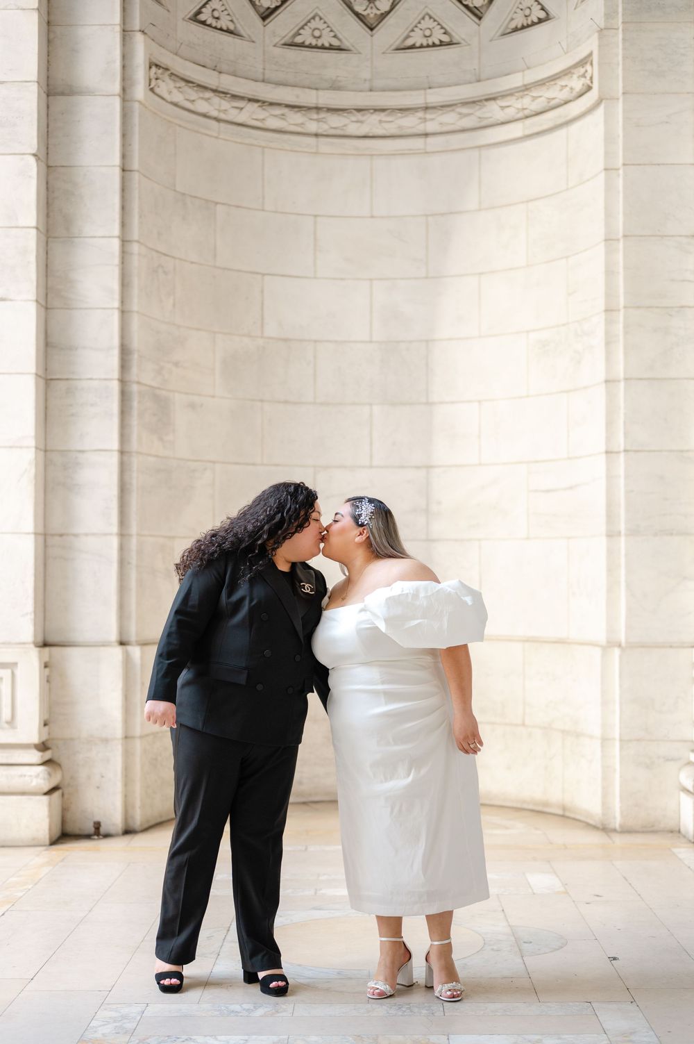 Two people share a romantic moment in front of an elegant white stone archway at NY Public Library during engagement session