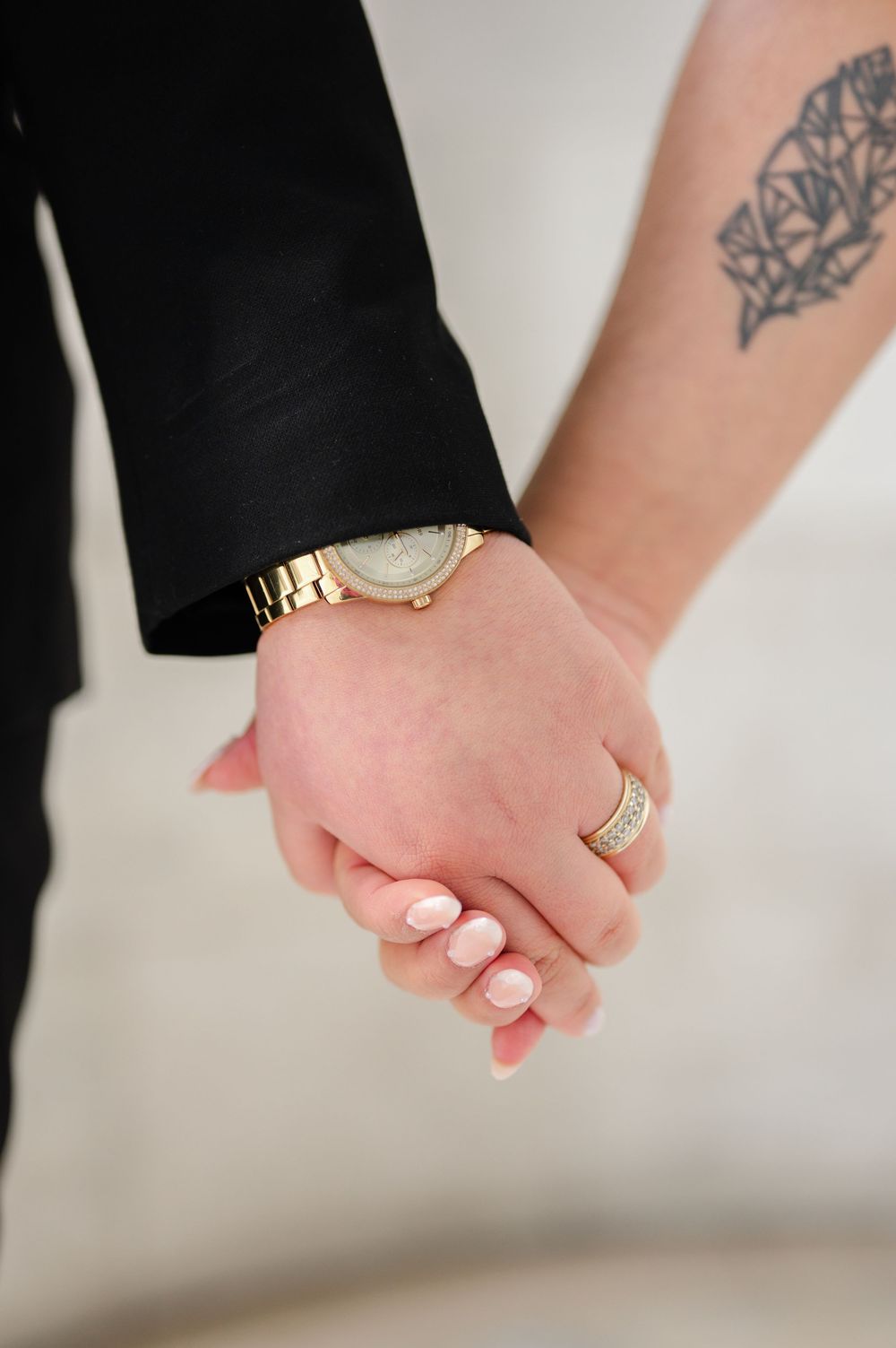 Close-up of two hands clasped together, with one wearing a gold watch and the other showing a geometric tattoo on the arm.