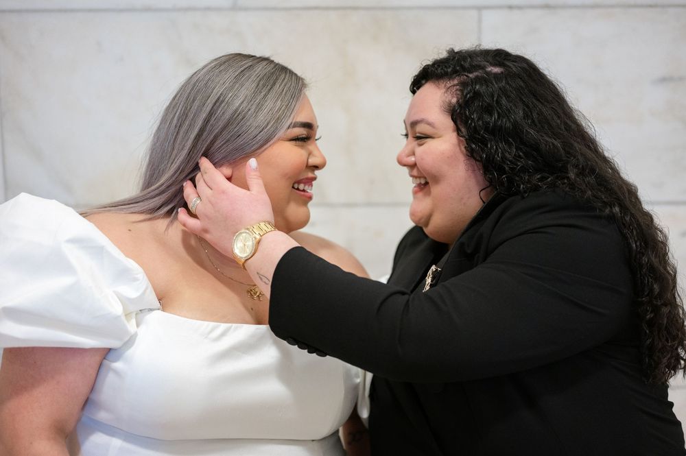 Two women share a joyful moment laughing together, one wearing white and one wearing black during engagement session