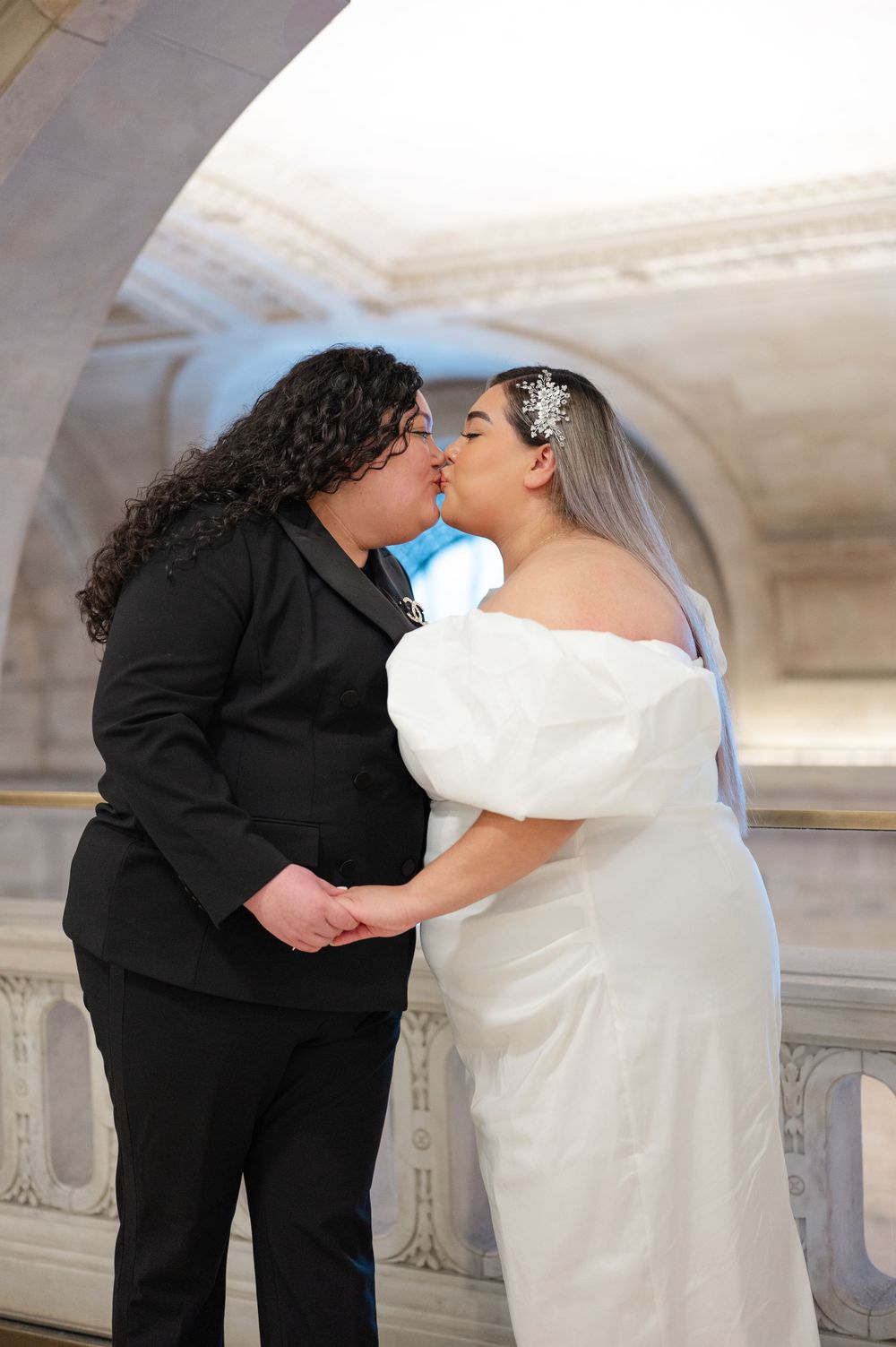 A romantic moment captured under an ornate stone archway between two people in contrasting black and white attire.