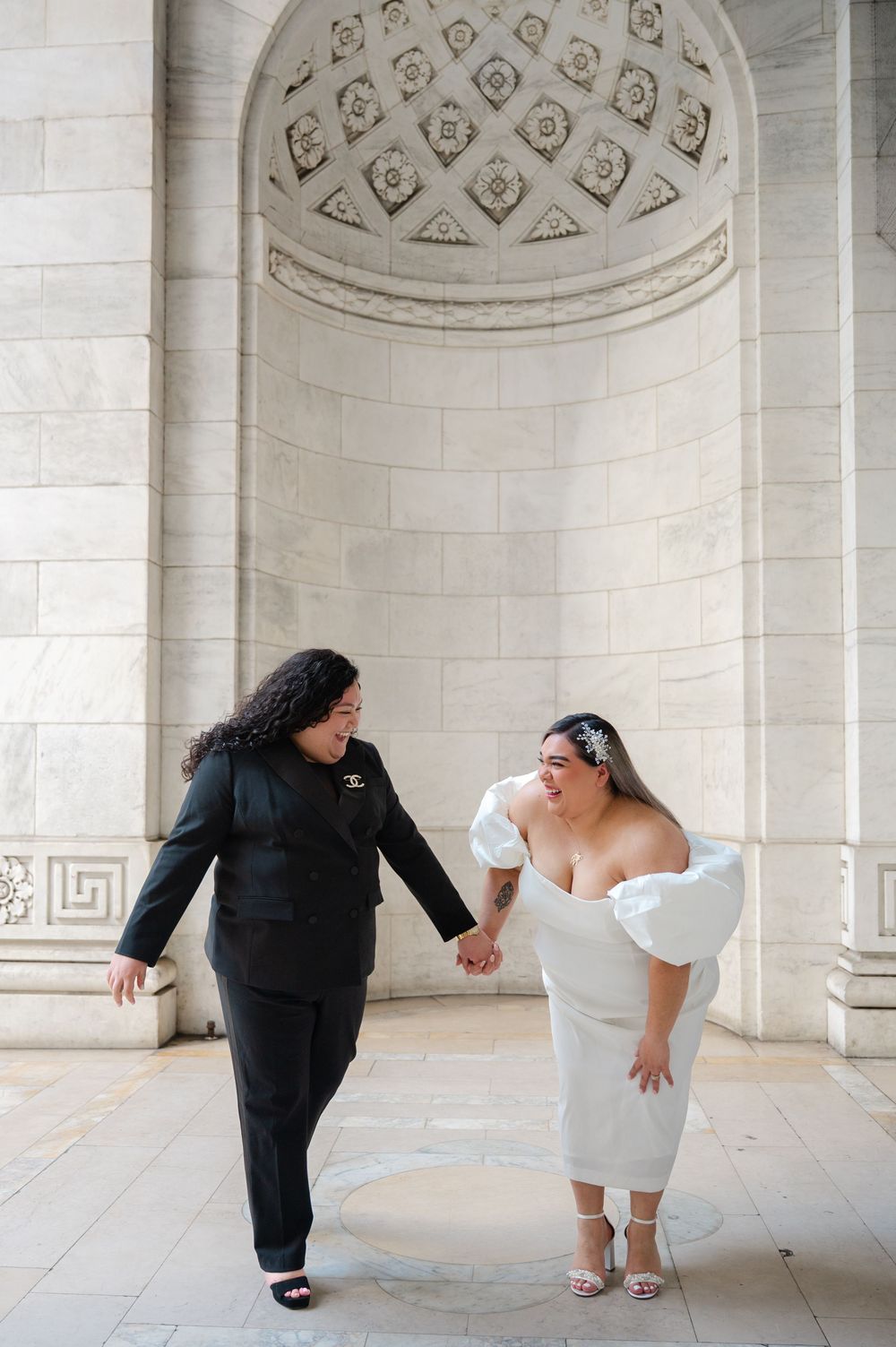 A couple shares a romantic moment in formal wedding attire under an ornate archway with decorative ceiling details at NY Public Library
