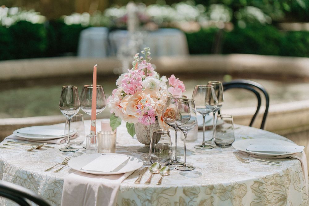An elegant table setting with pink floral centerpiece, crystal glasses and white linens at a garden reception.