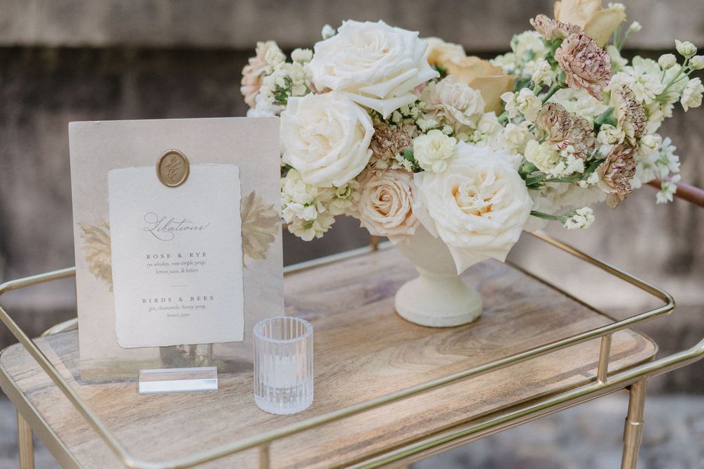 An elegant wedding invitation display with white roses and delicate florals on a gold mirrored tray.