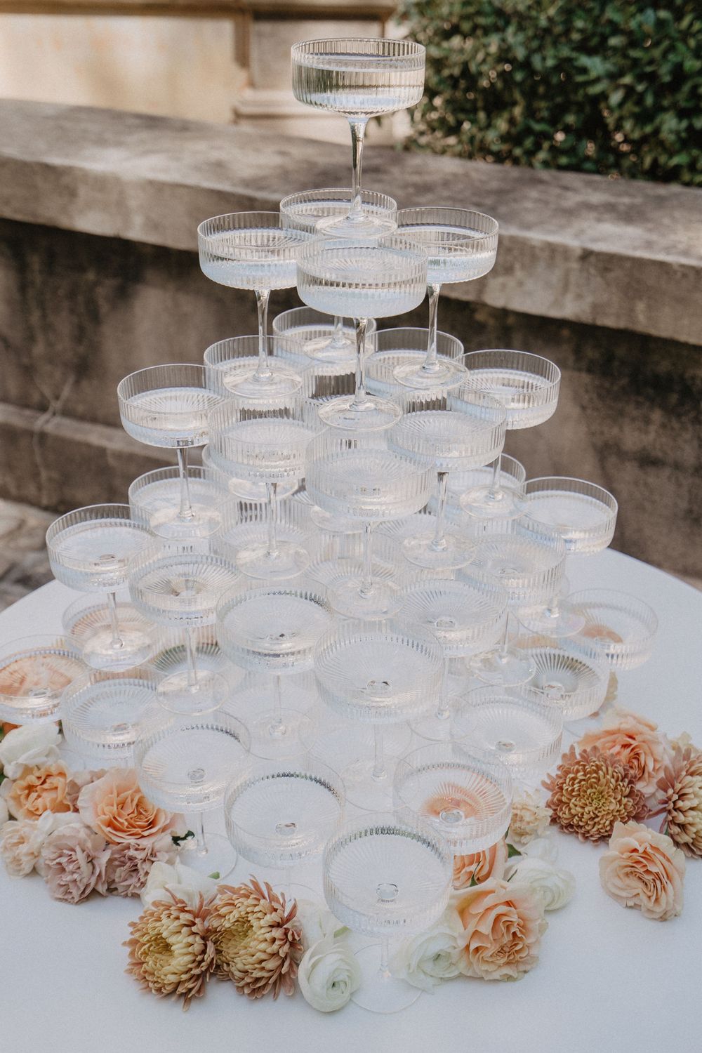 Champagne tower display decorated with peach and blush colored flowers.