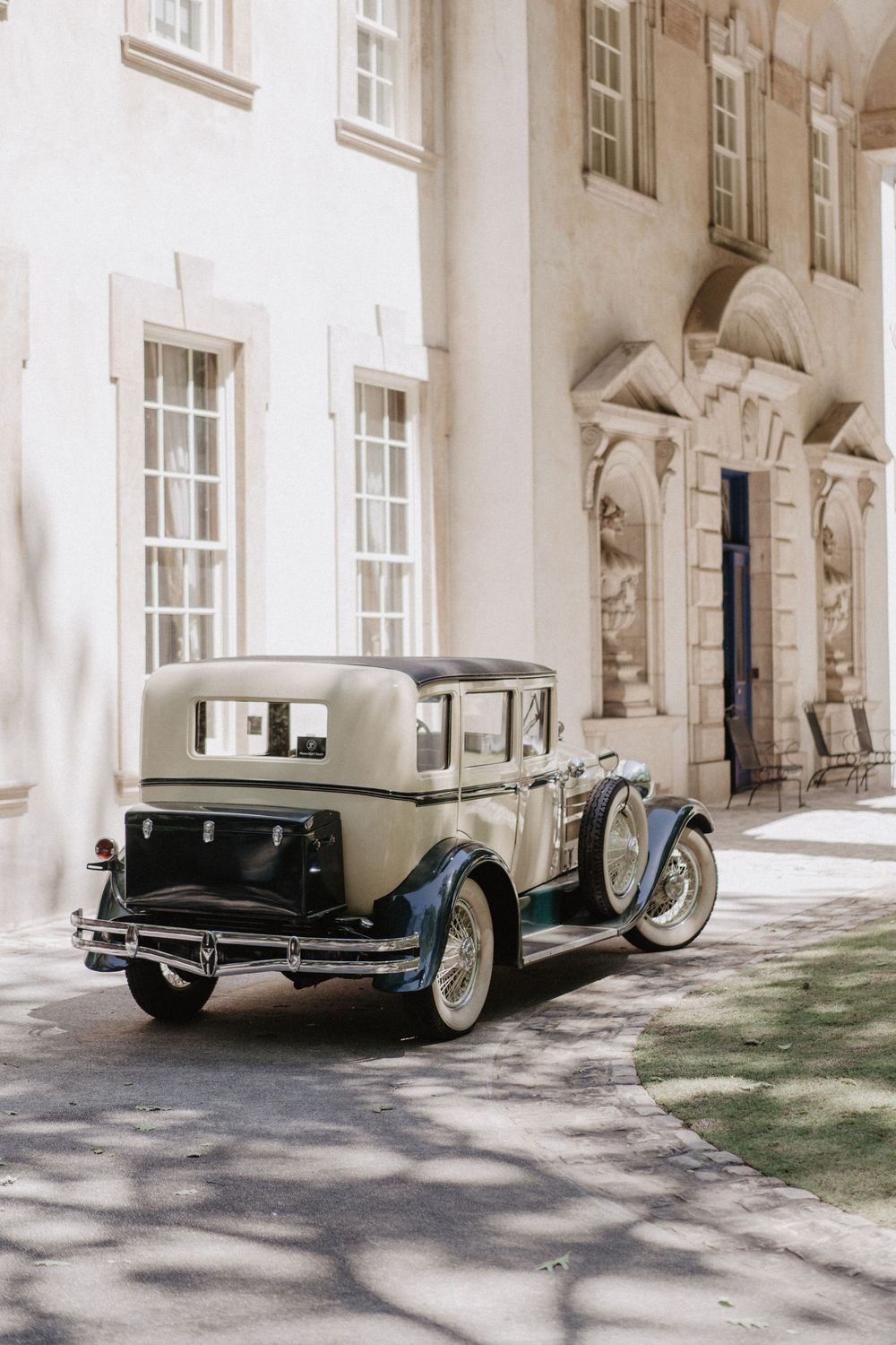 A vintage luxury car parked outside a grand classical building with arched doorways and windows.