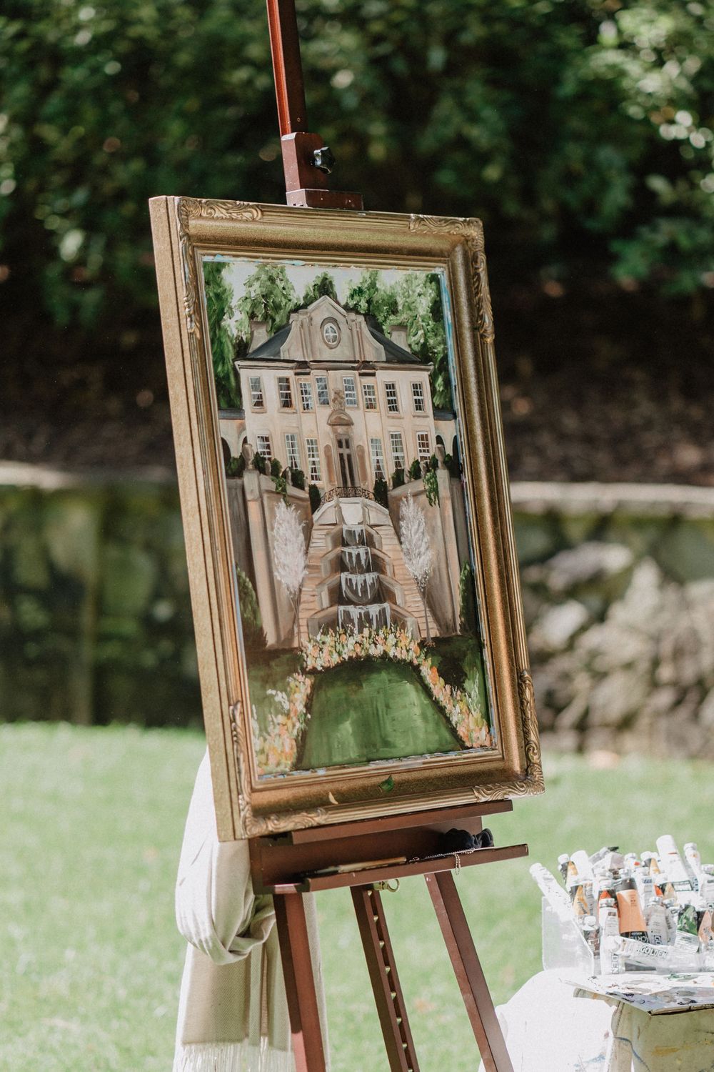 Framed watercolor painting of a grand mansion displayed on wooden easel outdoors.