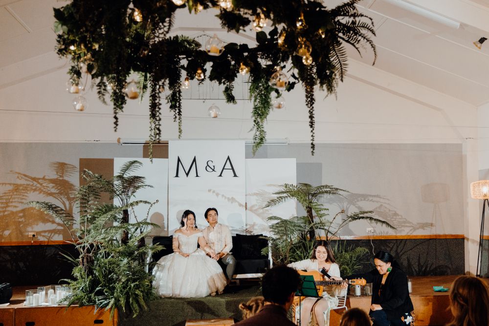An elegant wedding reception venue with hanging greenery and M&A signage on white backdrop.