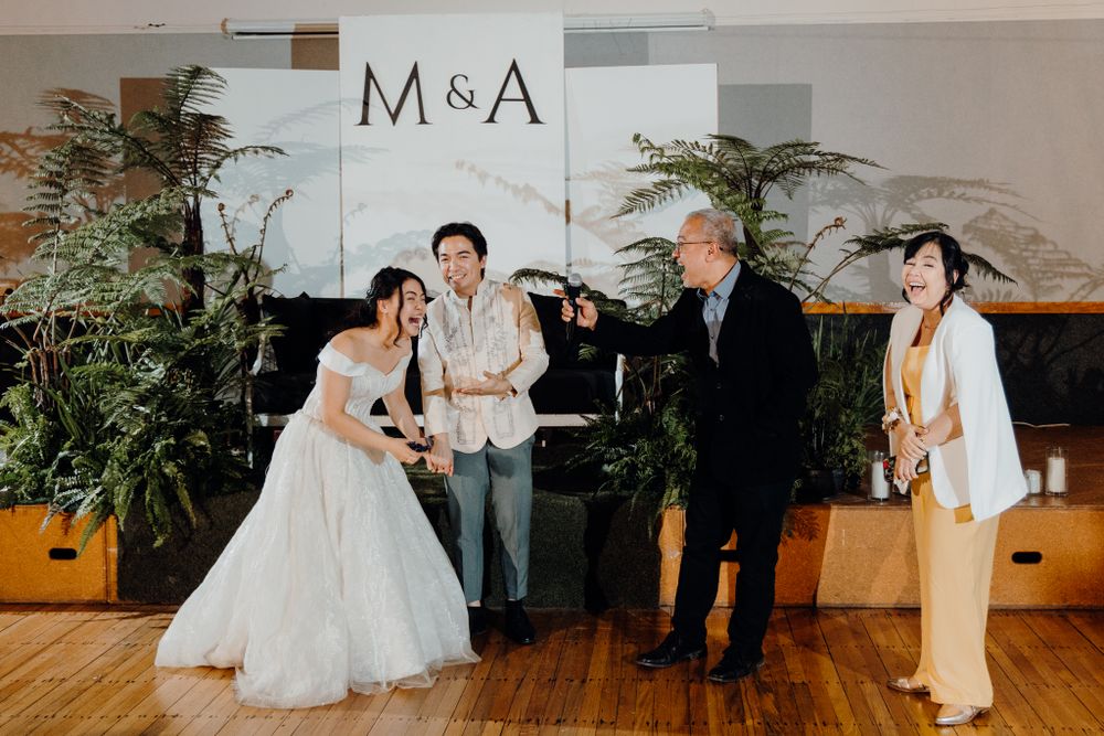Wedding celebration candid moment with guests and newlyweds in front of M&A backdrop.