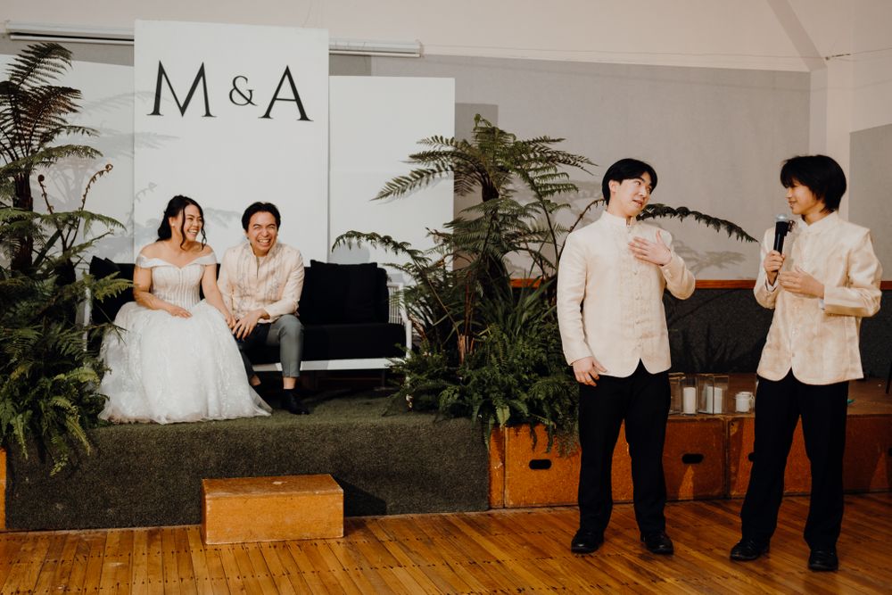 Wedding reception scene with piano and fern decorations against white backdrop with M&A signage.