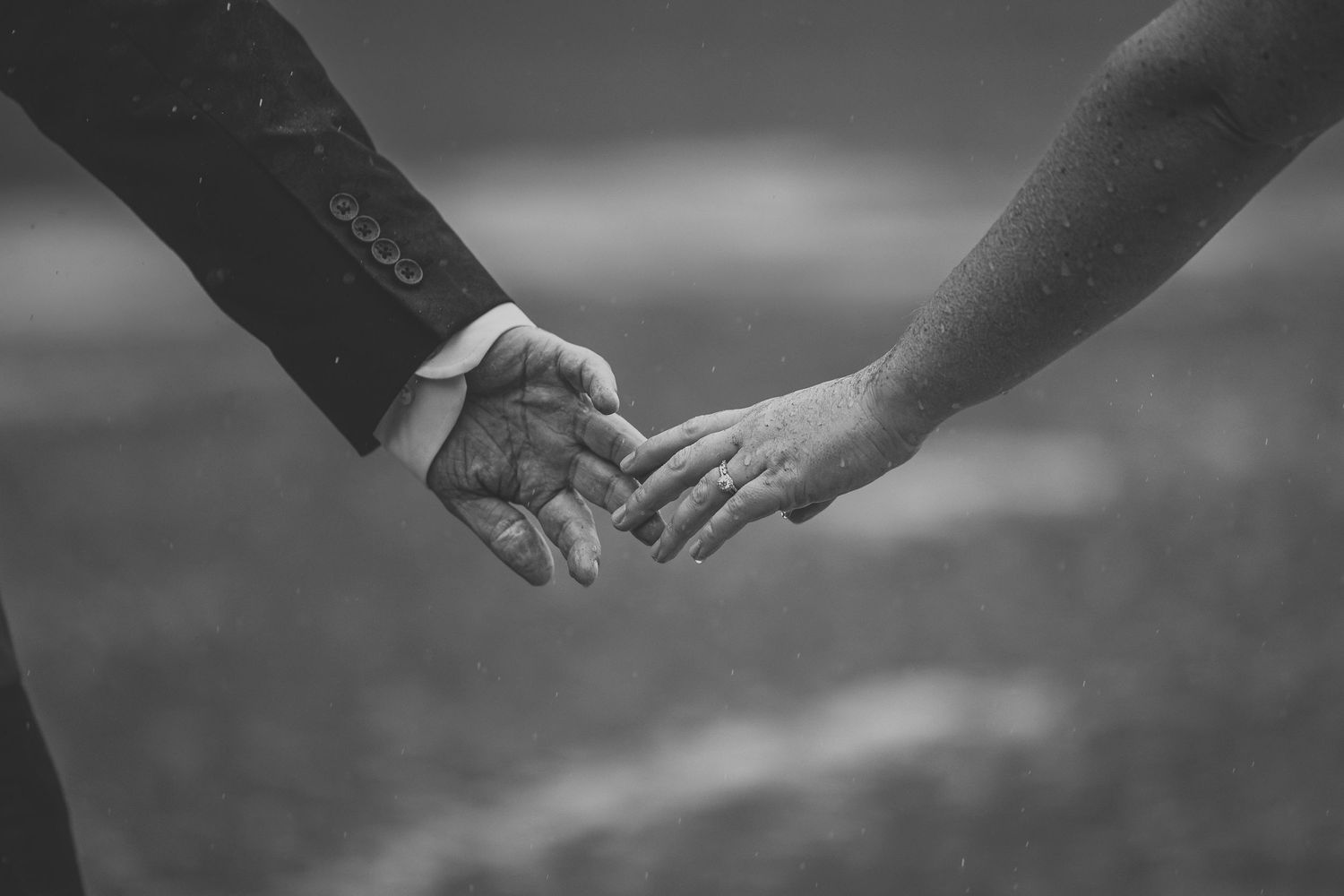 Black and white photo of two hands reaching out to touch each other against a blurred background.