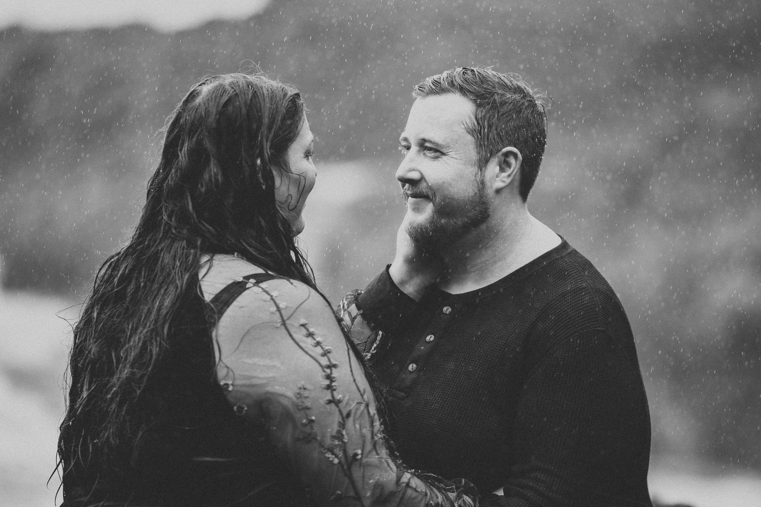 A black and white romantic portrait of a couple sharing an intimate moment while looking at each other and smiling.