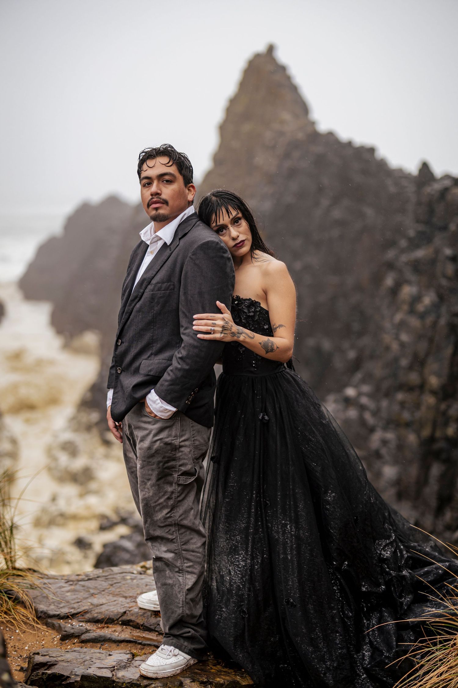 A couple poses dramatically against misty mountain peaks, with the woman wearing an elegant black gown.