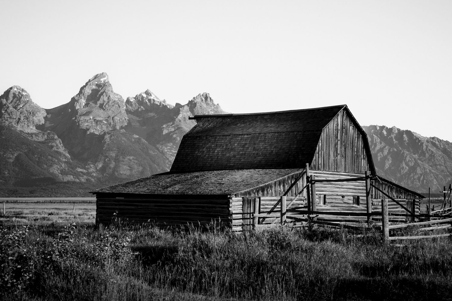 Rustic wooden barn beneath dramatic mountain peaks in black and white photography. mormon row in Teton national park