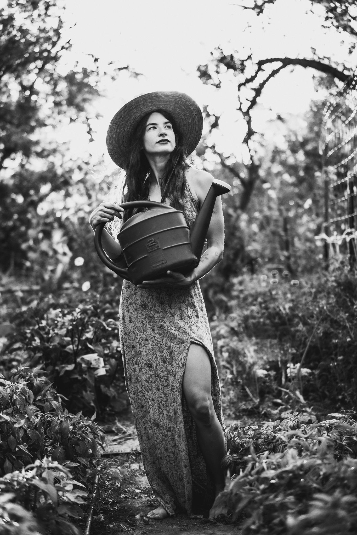 Artistic portrait of a figure in a sun hat holding a watering can in a garden setting.