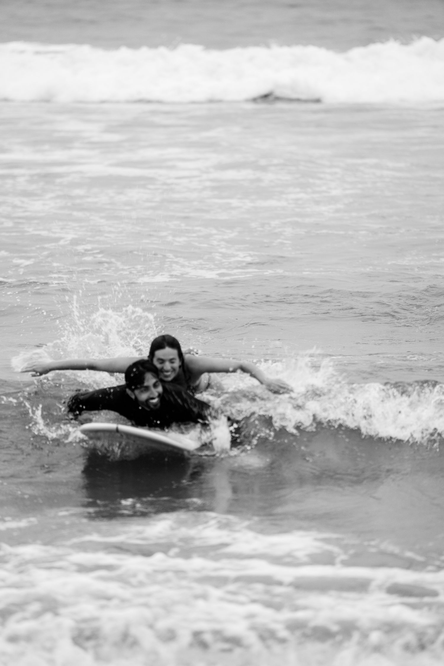 Two surfers riding a wave together during a beach day captured in black and white.