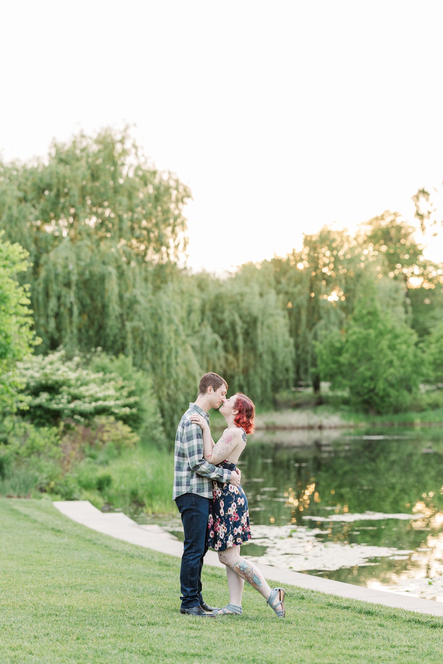 Romantic couple standing by tranquil pond with weeping willow trees at sunset in a peaceful park setting at Cantigny Park