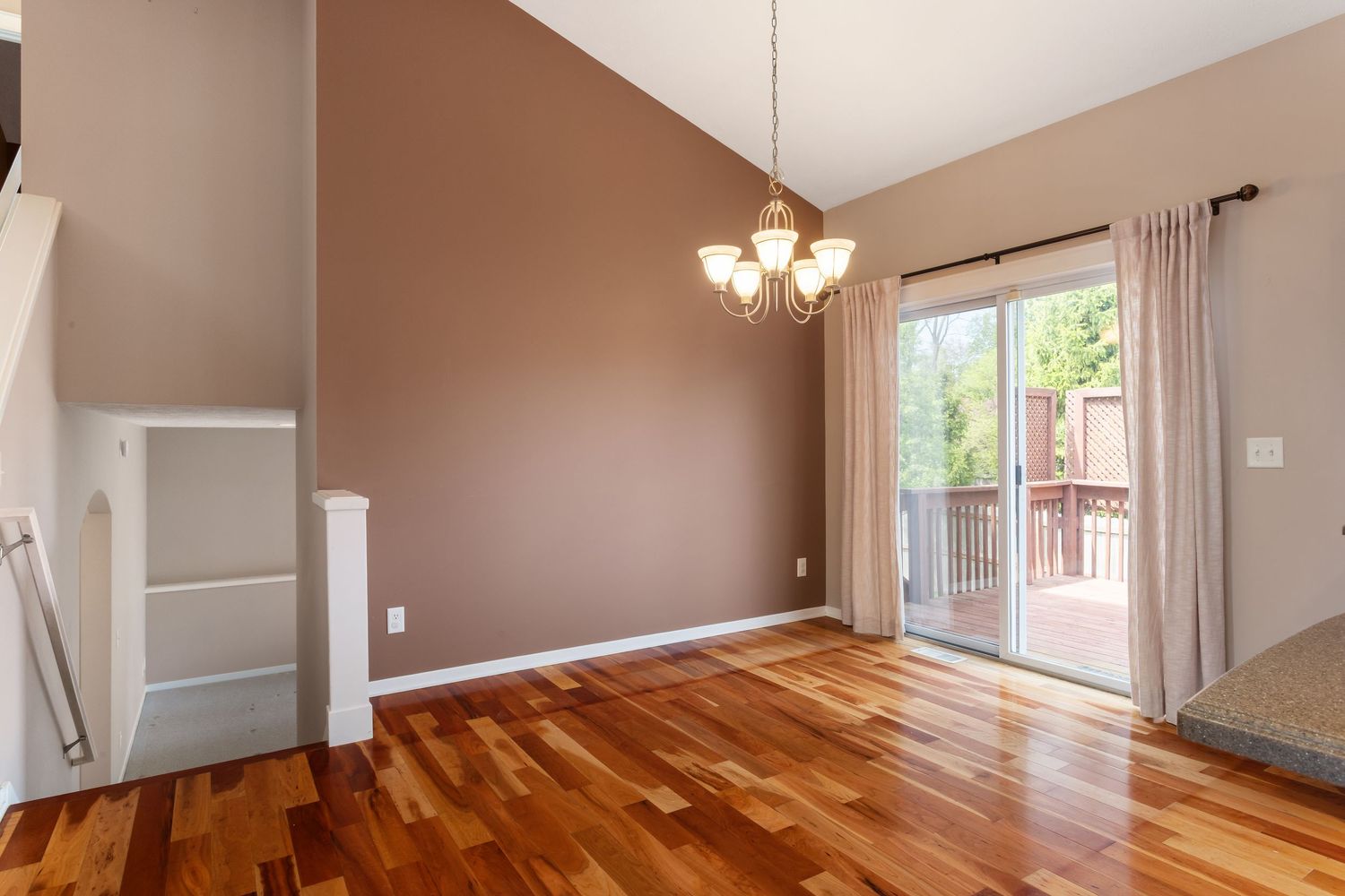 Bright room with brown accent wall, hardwood floors, and sliding glass door leading to outdoor deck.