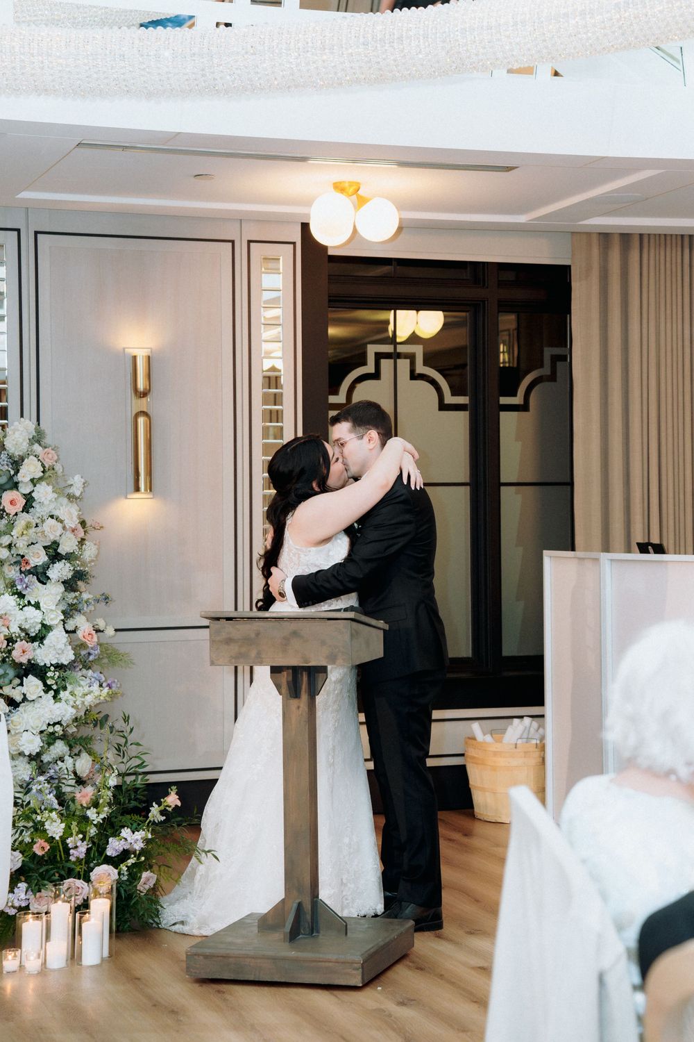 A tender moment shared at a wedding ceremony with a wooden podium against elegant decor.