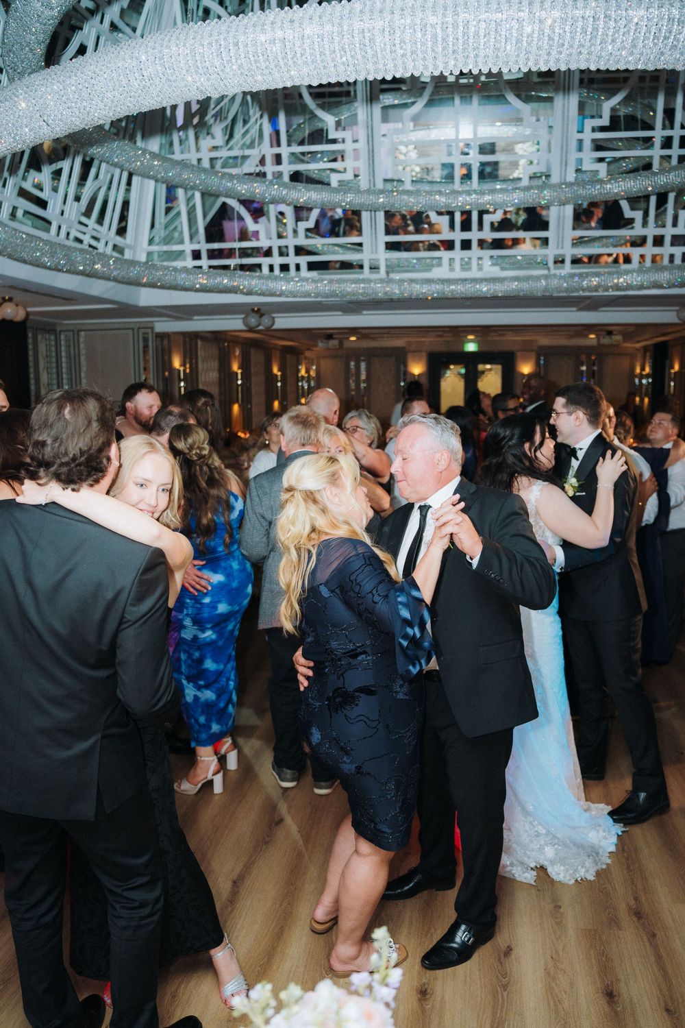 Wedding guests dancing and socializing on a wooden dance floor under industrial-style ceiling decor.