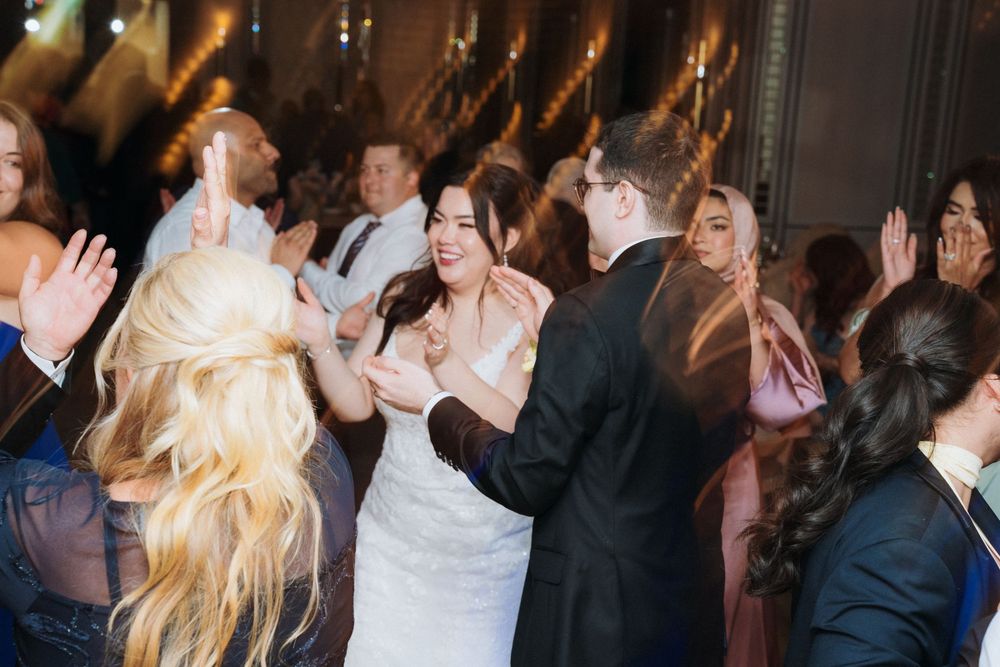 Wedding reception dance floor filled with celebrating guests under decorative lighting.