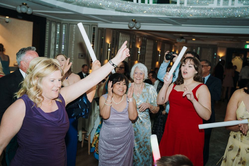 Enthusiastic wedding guests dancing and celebrating with glow sticks on the dance floor.