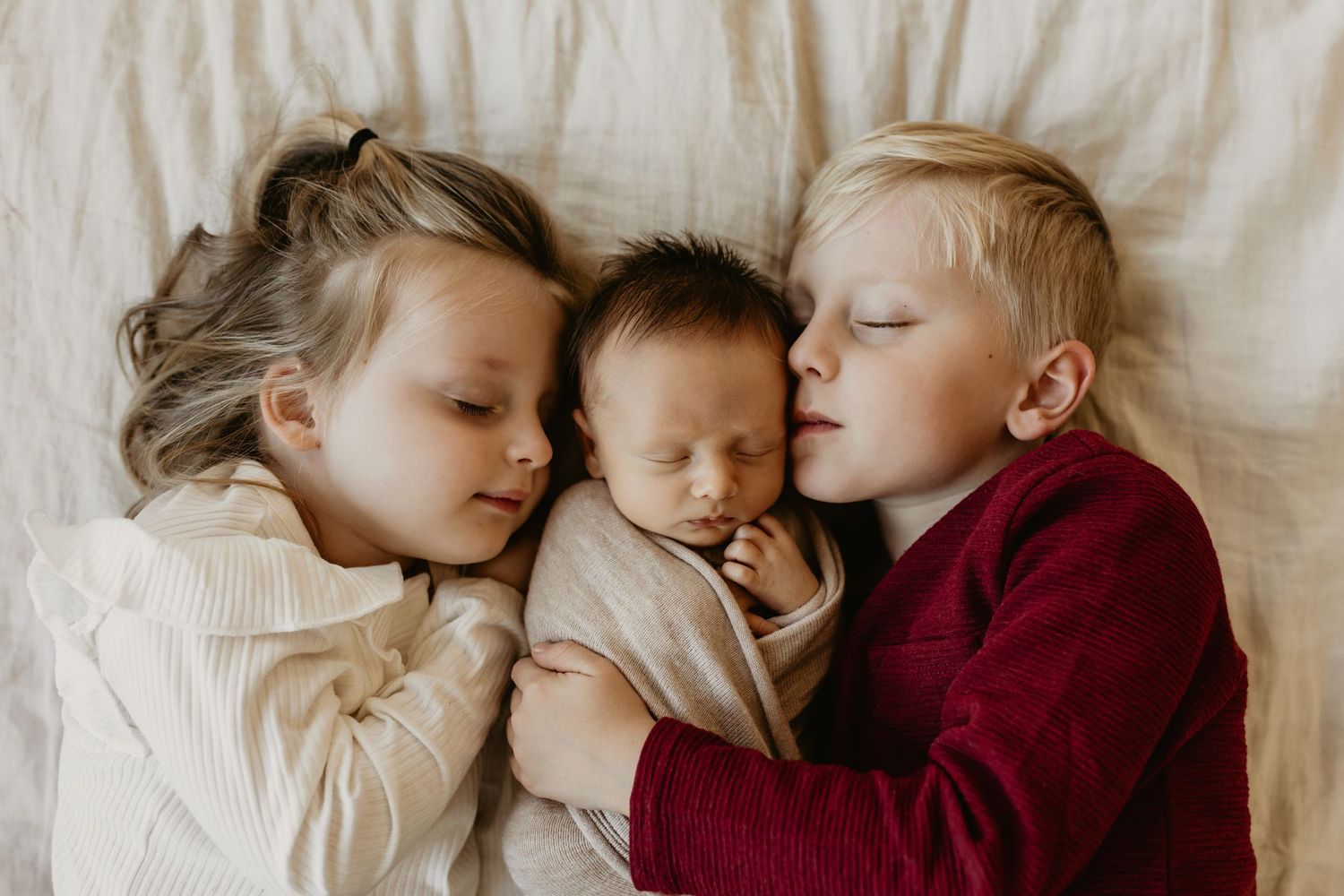 Three siblings snuggle close together on white bedding, Tulsa newborn photographer