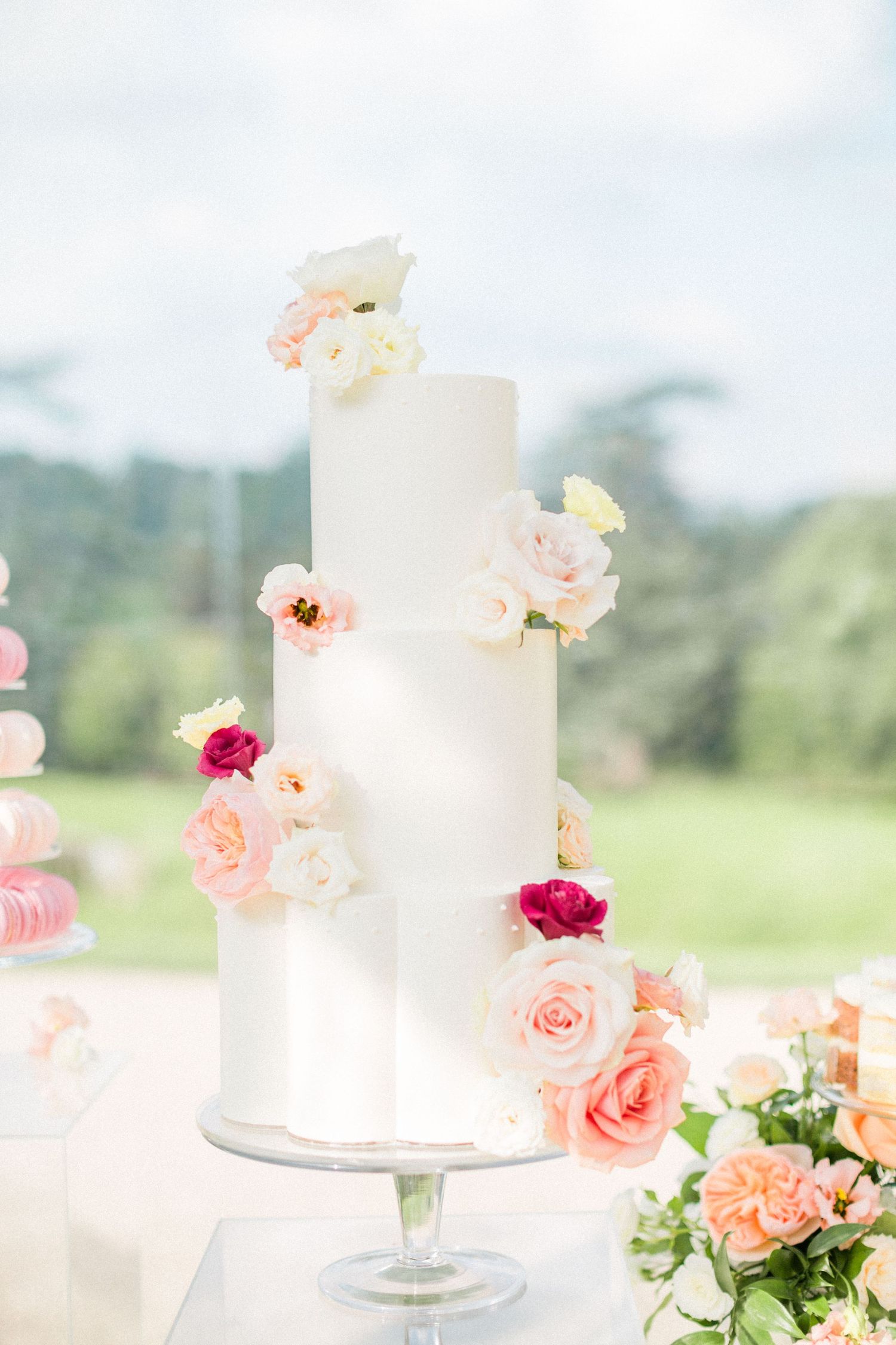 White wedding cake decorated with delicate pink garden roses, deep pink blooms and peachy-coral flowers against a soft backdrop at Sezincote