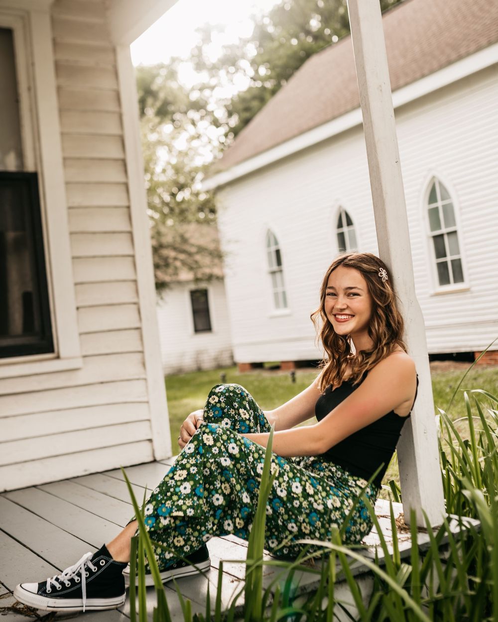 Relaxed outdoor portrait on a porch with white church buildings in the background.