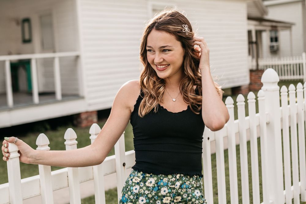 Casual summer pose by a white picket fence wearing a black top and floral skirt.