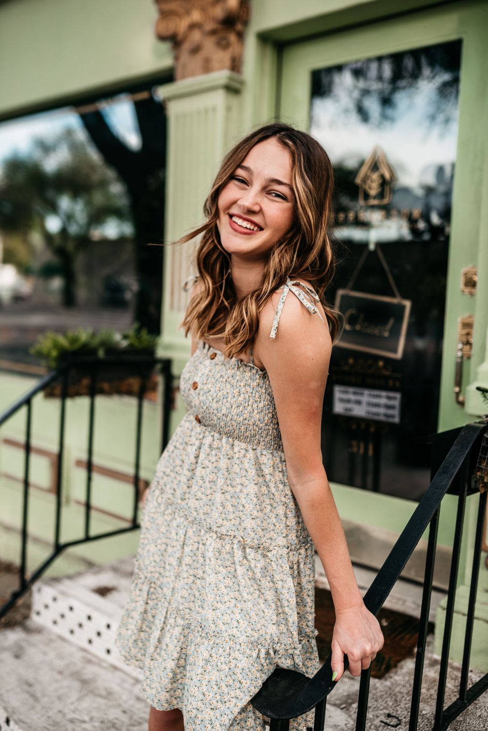 Candid portrait in a sparkly beige summer dress against a mint green building exterior.