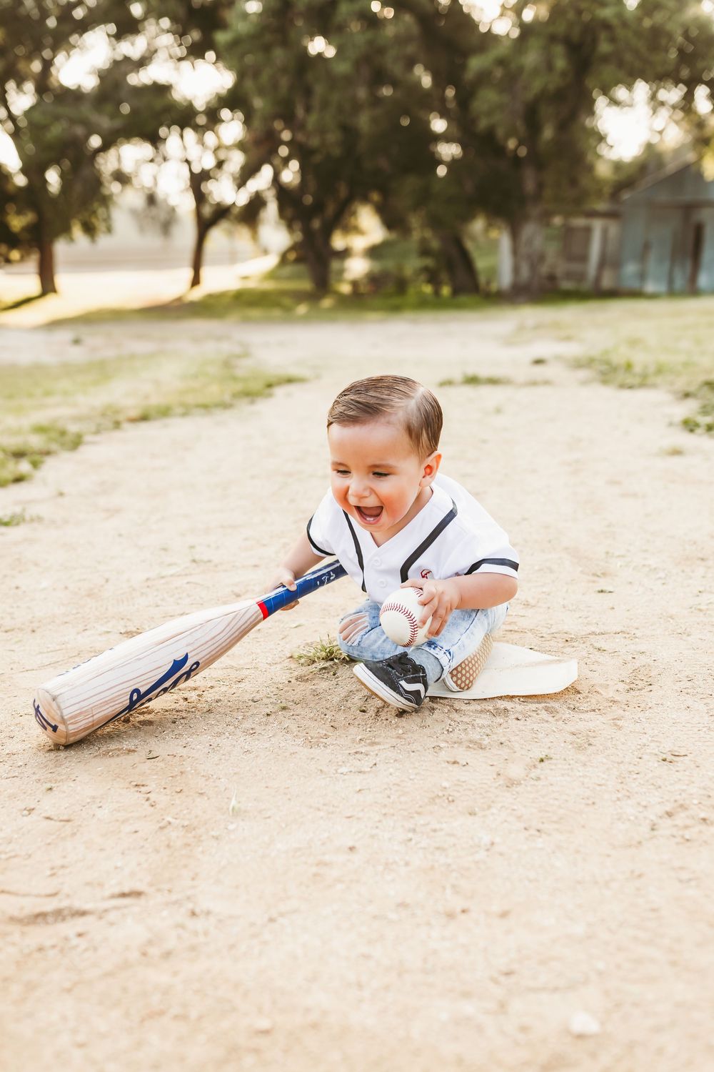 A baseball player in white uniform slides across dusty ground during game action at field.