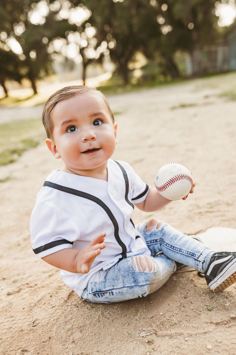 A baby in a white sailor outfit lies on sand while holding a baseball in triptych style photo series.