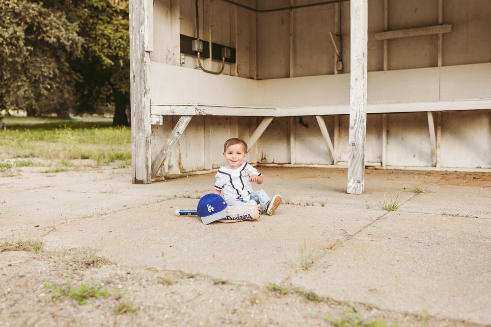A small child sits on concrete under a white wooden stage or platform structure in an outdoor setting.