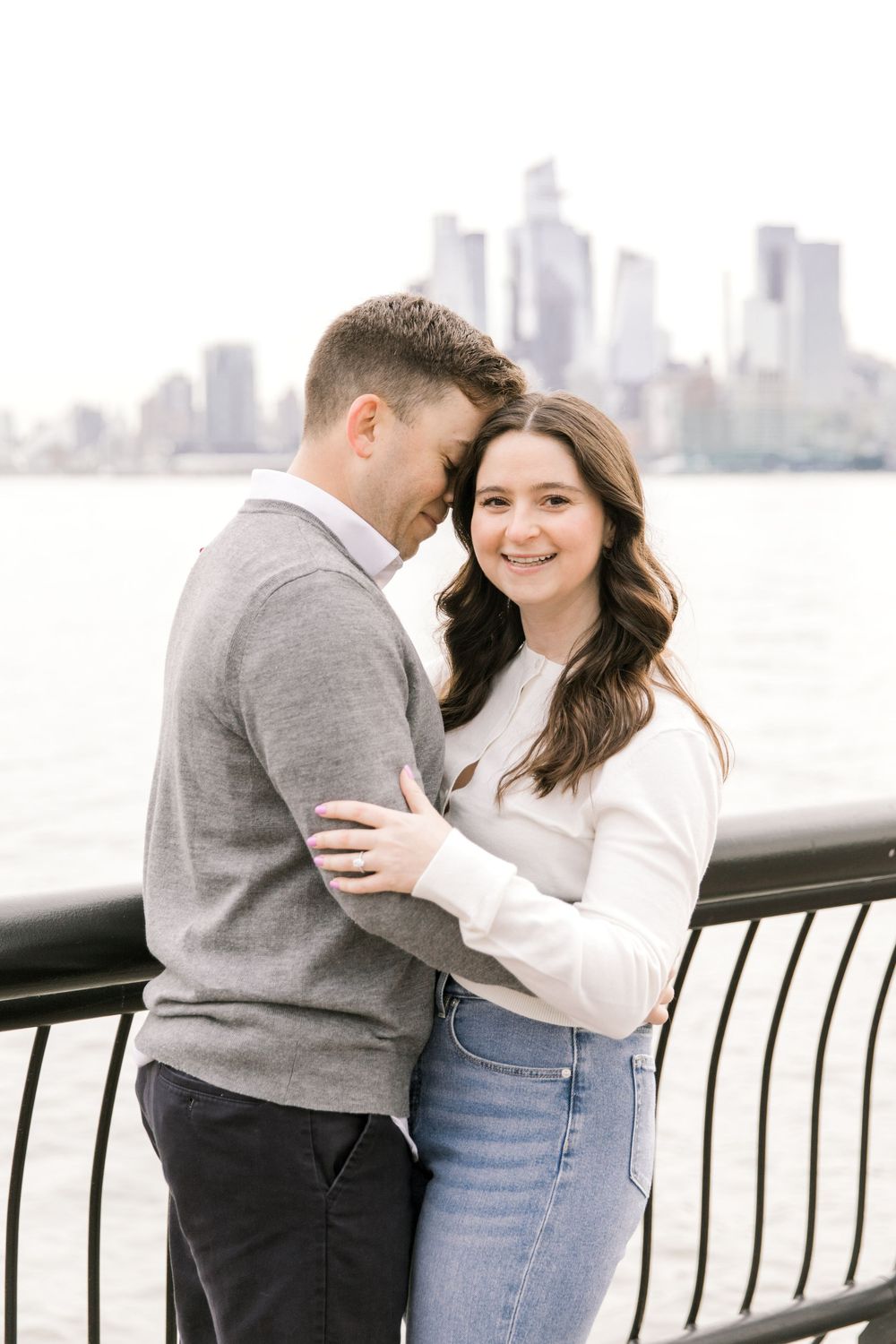 Engaged couple sharing a romantic moment with Manhattan skyline views at Pier A Park.