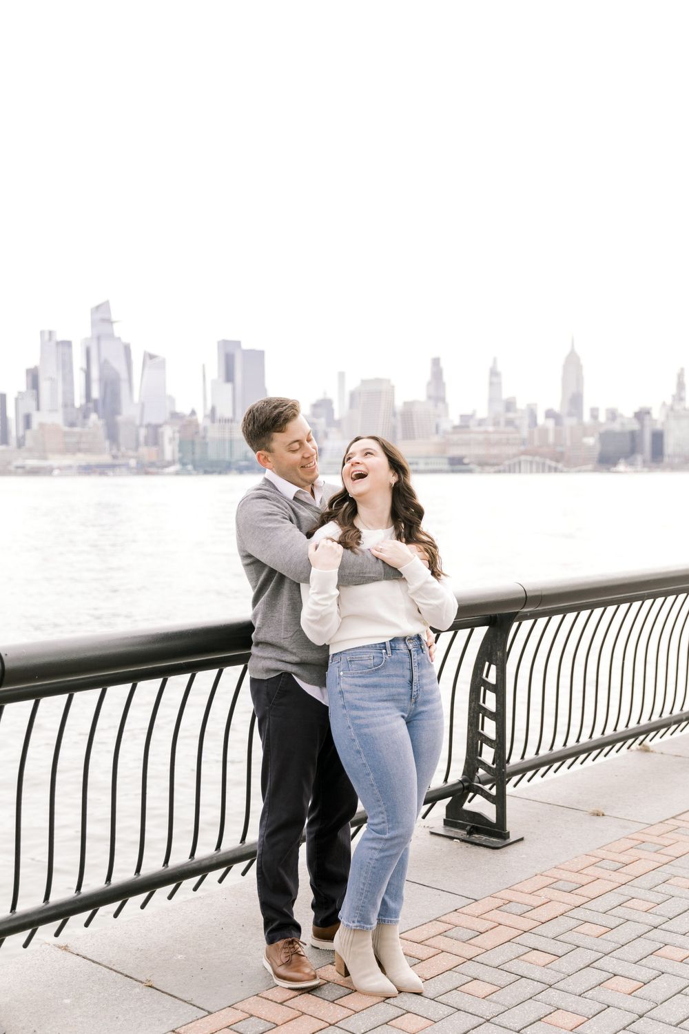 Engaged couple sharing a romantic moment with Manhattan skyline views at Pier A Park.