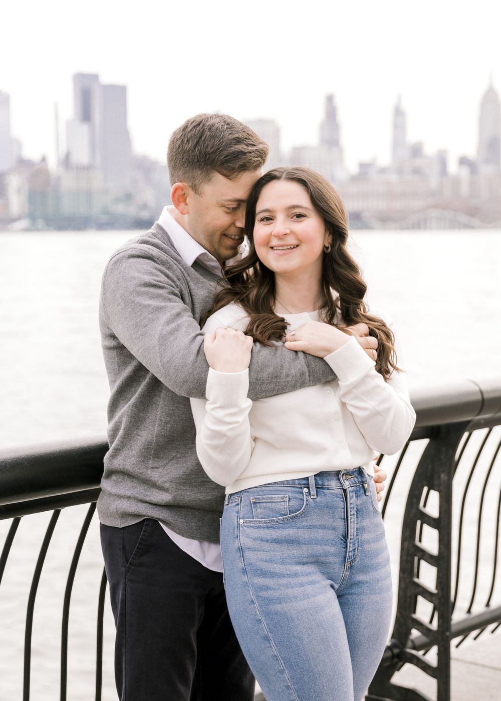 Engaged couple sharing a romantic moment with Manhattan skyline views at Pier A Park.