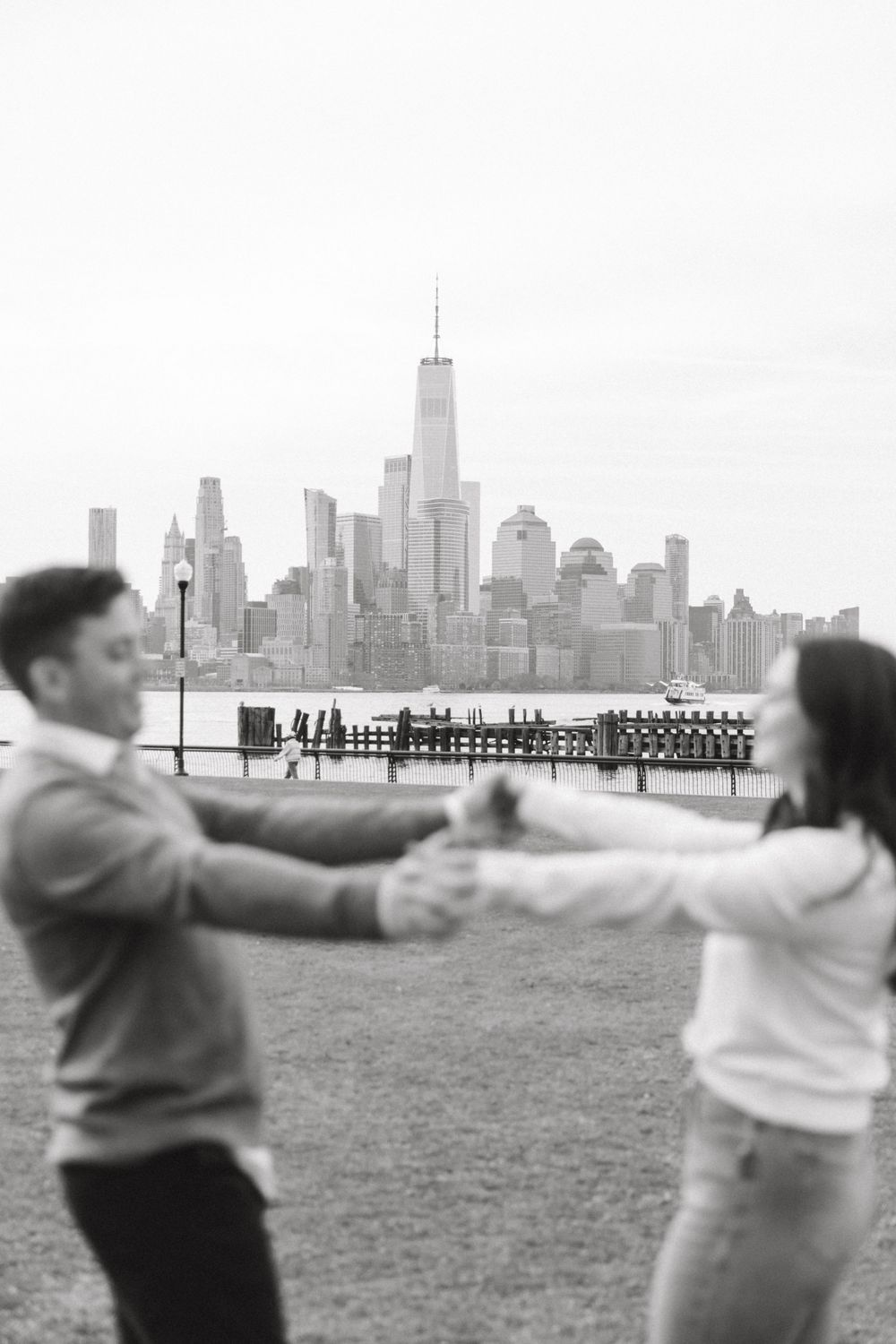 Engaged couple sharing a romantic moment with Manhattan skyline views at Pier A Park.