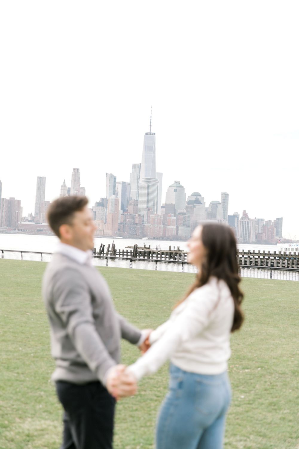 Engaged couple sharing a romantic moment with Manhattan skyline views at Pier A Park.
