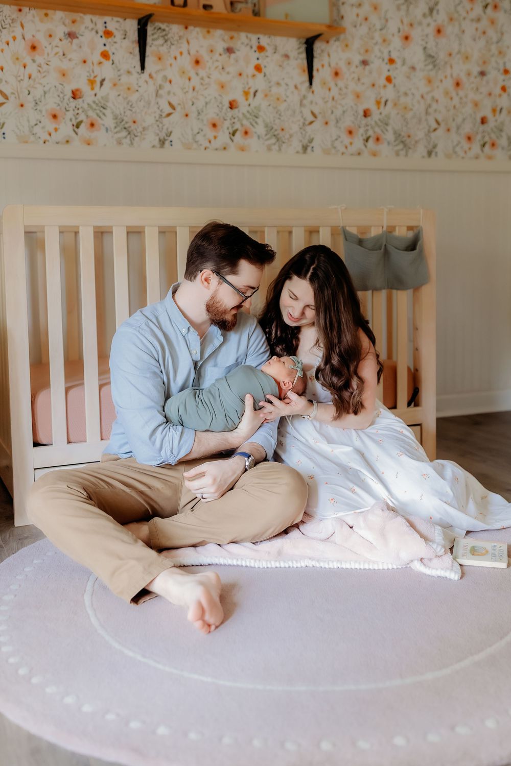 Family sharing tender moments while lying together on bed with floral wallpaper in background.