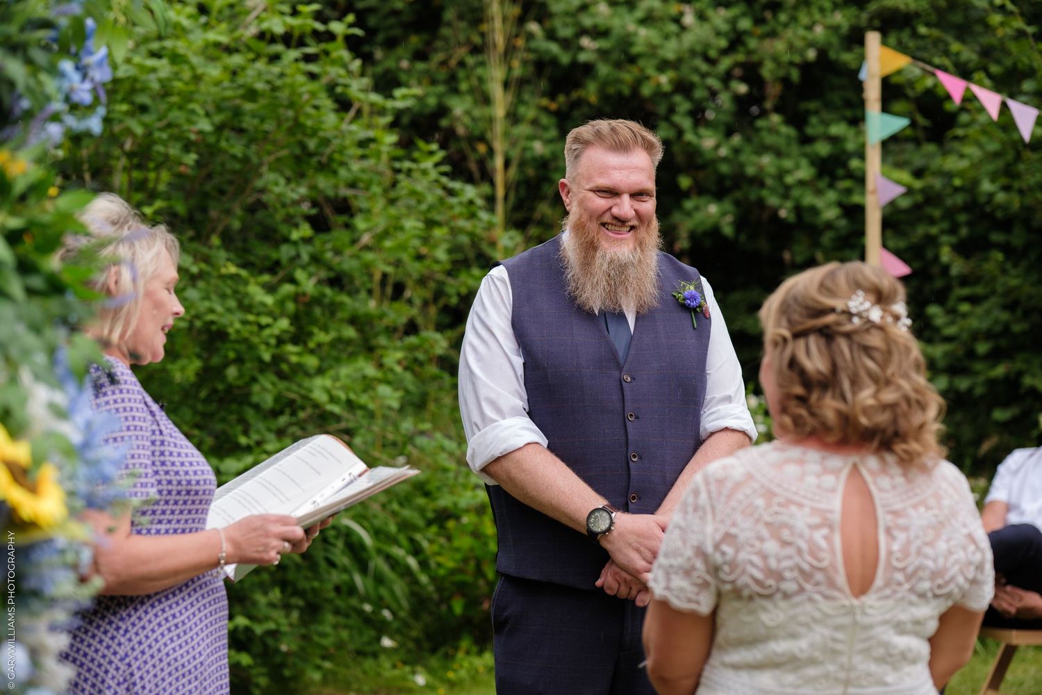 Outdoor wedding ceremony in a lush garden setting with attendees gathered during an afternoon celebration.