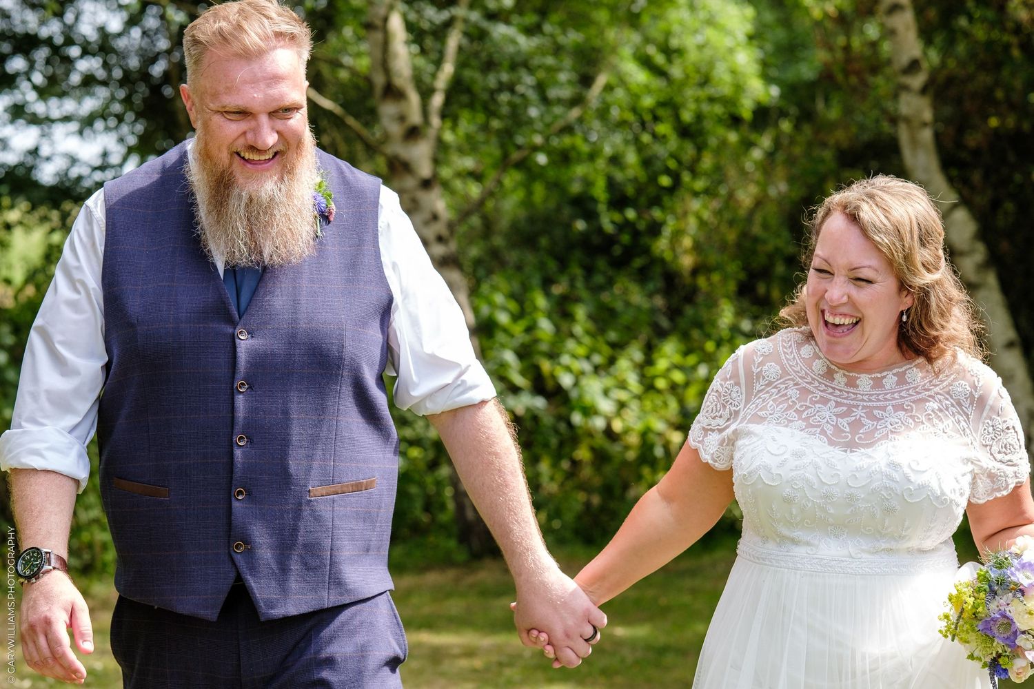 A joyful couple holding hands and laughing together outdoors on their wedding day.