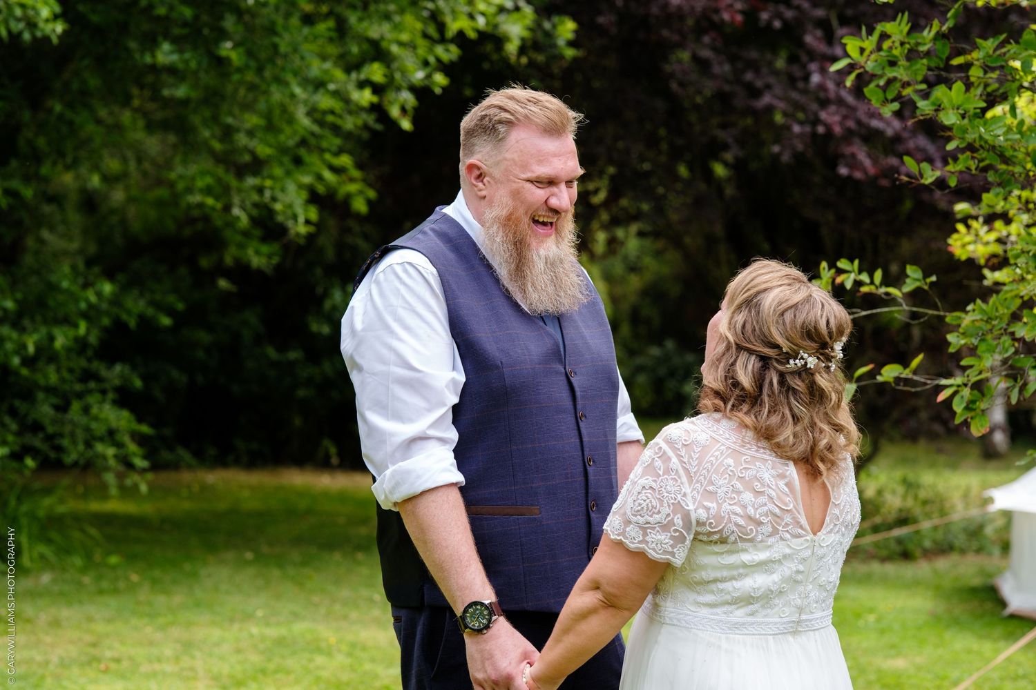 Couple in casual wedding attire holding hands and smiling at each other in a garden setting.