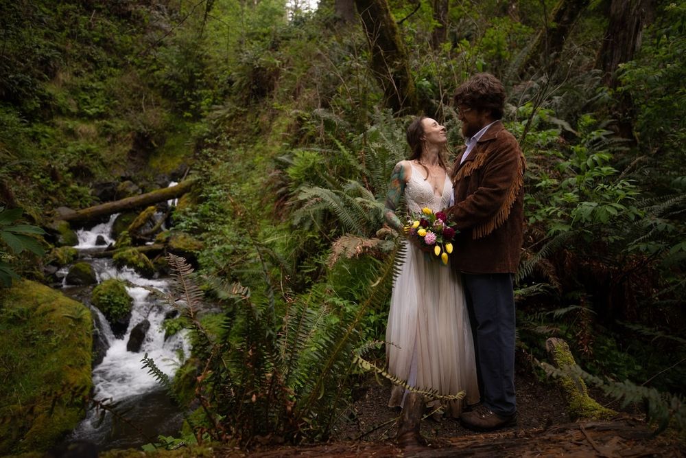 couple standing by a waterfall in wedding attire on Oregon coast