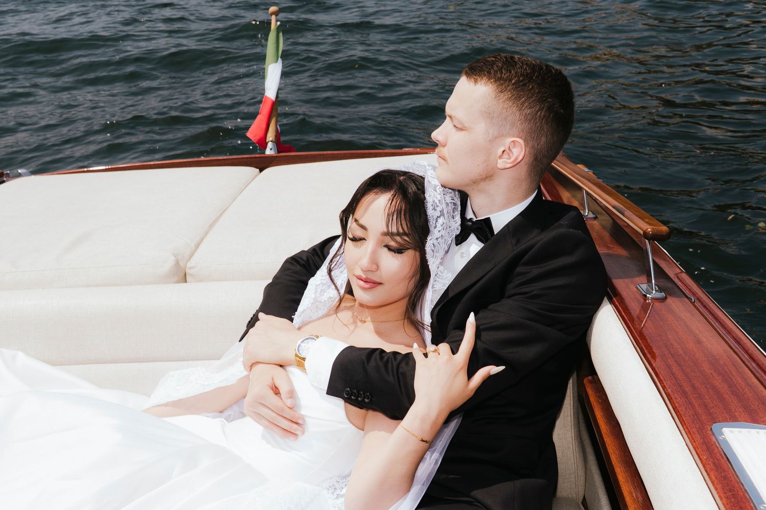 Elegant couple aboard a vintage wooden boat basking in sunlight on calm waters.