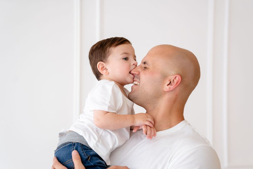 An intimate moment captured between a parent and child sharing a playful kiss against a white background.