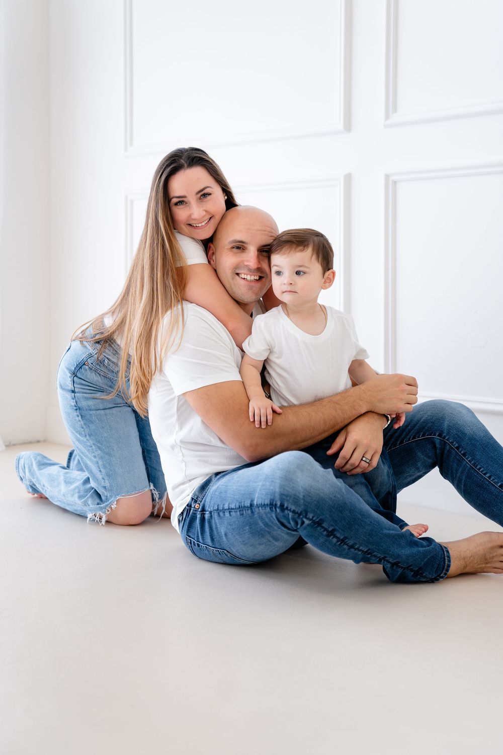 A loving family portrait shows three people hugging while sitting together on a bright white floor.