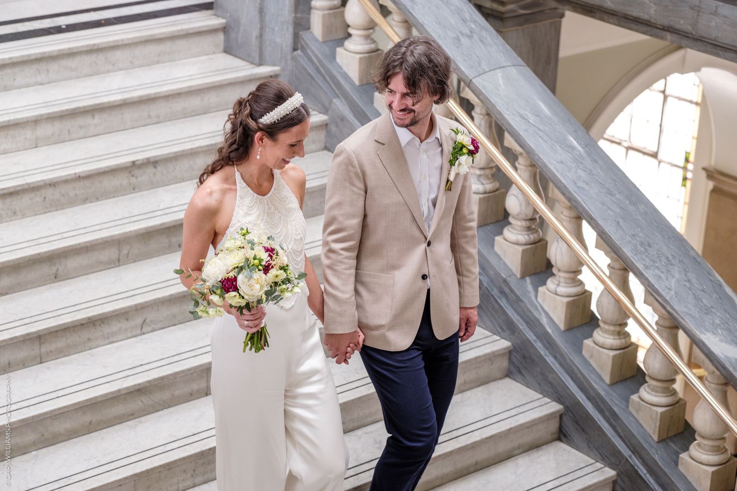 A couple shares an intimate first look moment in a hallway decorated with framed artwork and white columns.