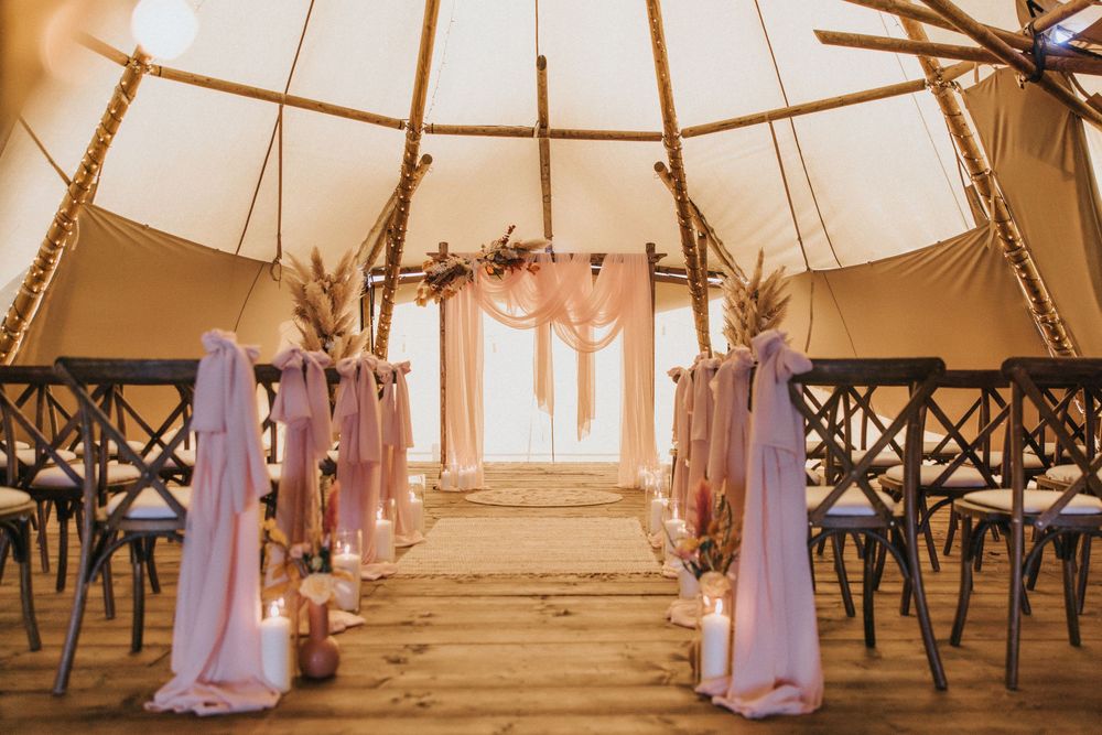 Rustic wedding aisle inside tipi tent with crossback chairs, draped fabric, and dried floral arrangements at Nuddock Wood Lake.
