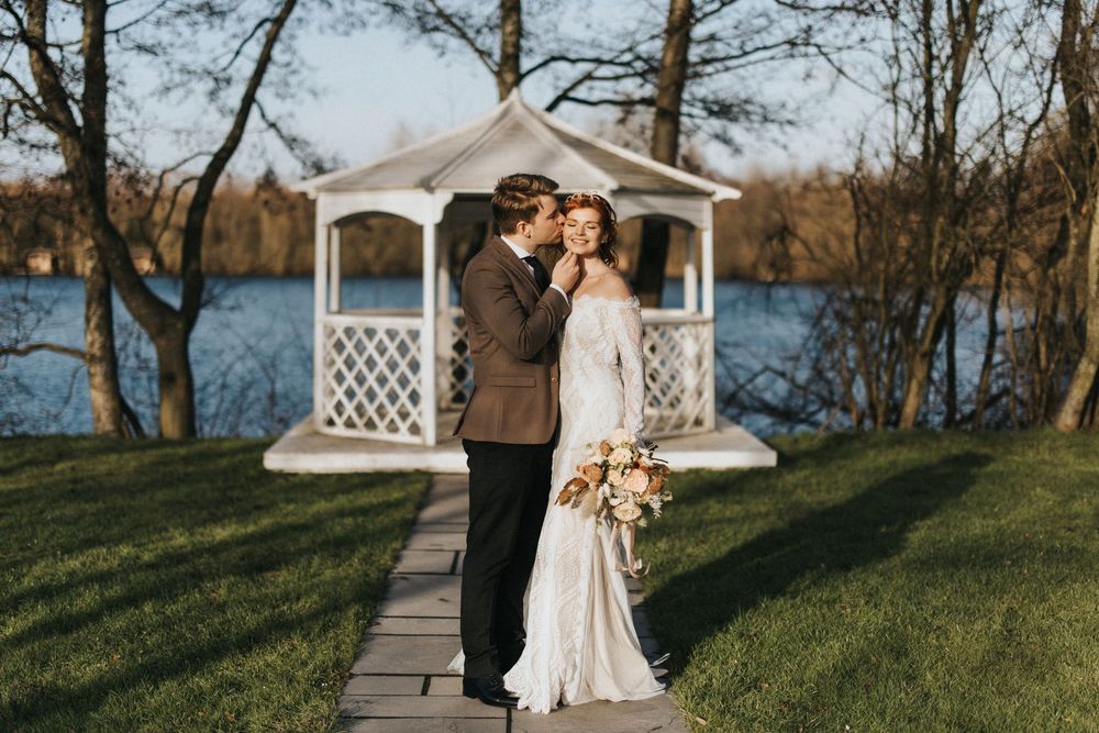 Newlyweds share romantic moments on a scenic hilltop overlooking a lake with white gazebos at Nuddock Wood Lake.